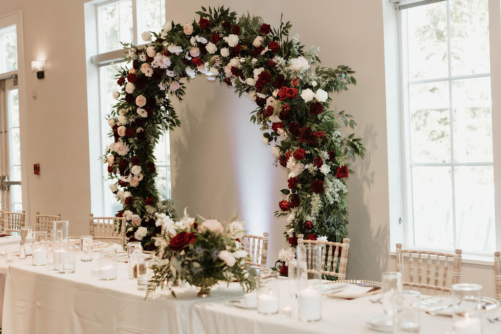Reception head table with white and red floral arch in background