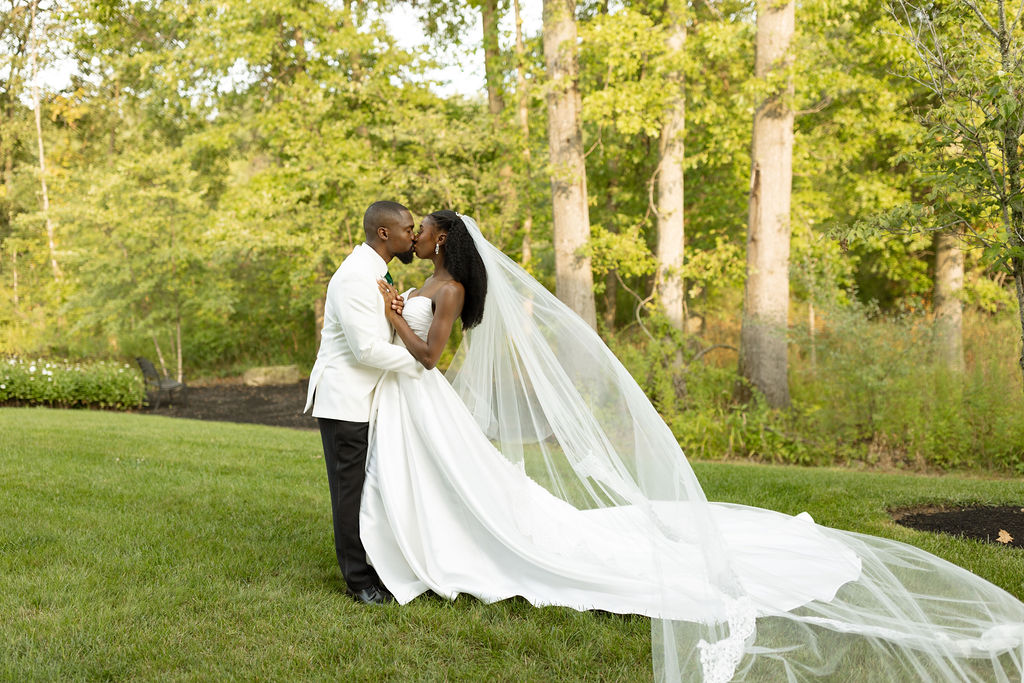 Newlyweds kissing in grass in front of trees and garden