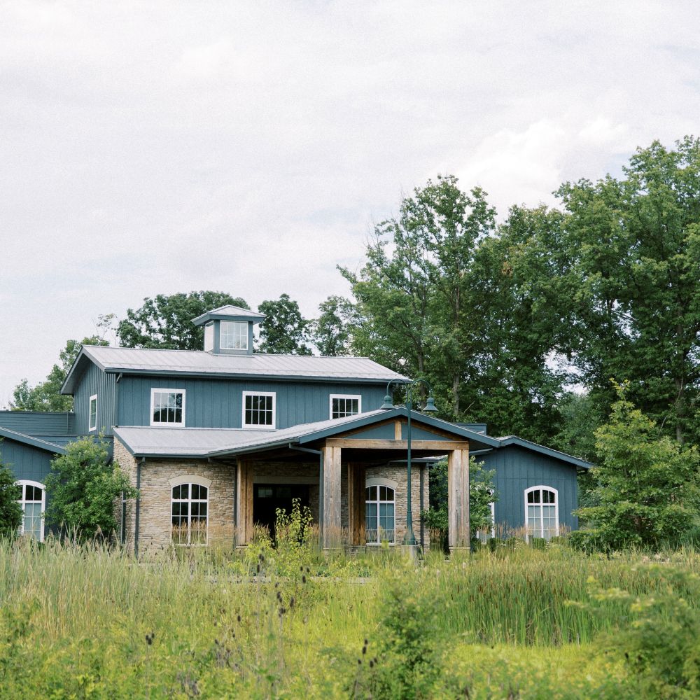 Exterior view of The Estate at New Albany, featuring a stone and blue siding façade surrounded by trees and natural landscaping.