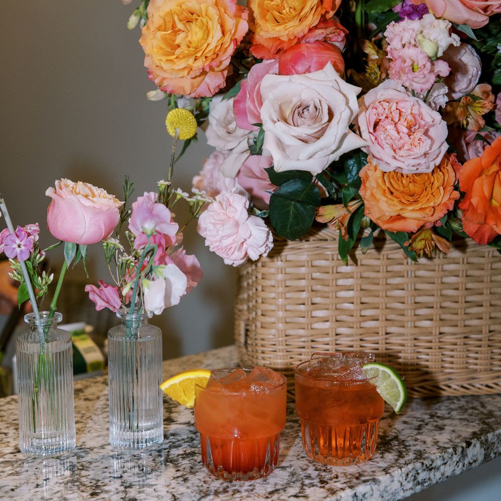 Colorful floral arrangement with pink and orange roses beside two cocktails garnished with citrus slices at The Estate at New Albany.