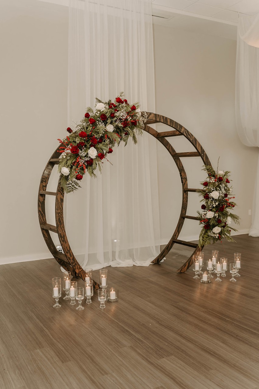 Floral wedding arch with candles in the Forest & Noble Rooms at The Estate at New Albany, featuring red and white flowers with greenery against sheer drapery.