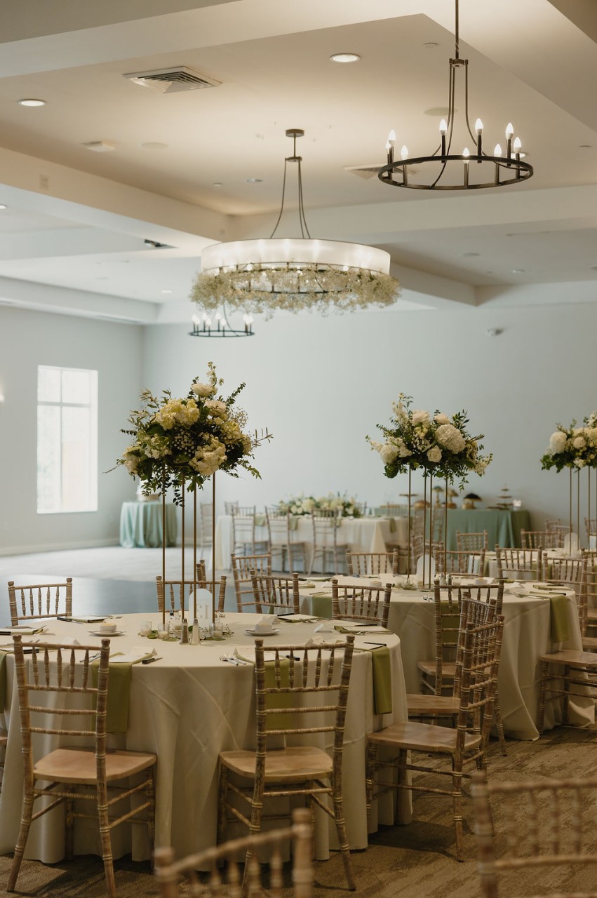 Wedding reception setup in the Great Hall at The Estate at New Albany, featuring round tables with tall floral centerpieces, chiavari chairs, and soft neutral linens.