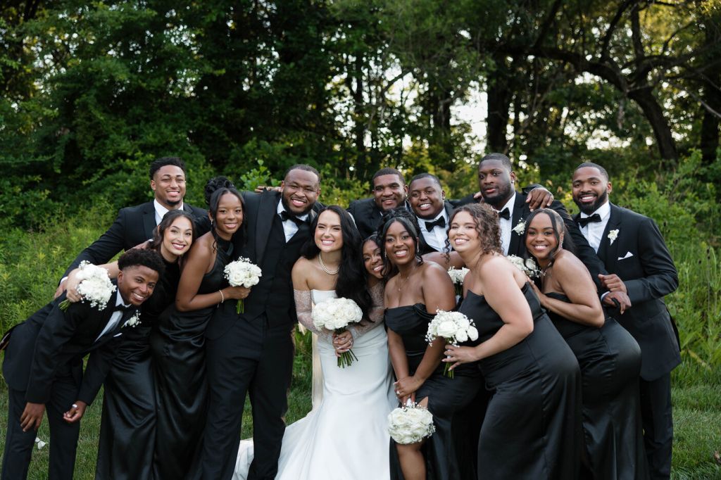 Newlyweds with bridal party in front of woods